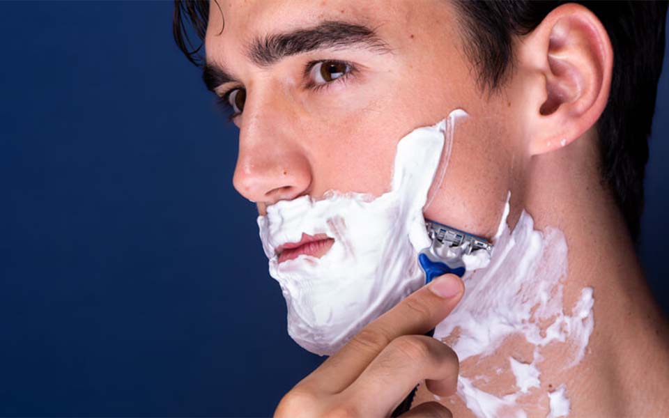 Ein Mann der sich mit einem Nassrasierer rasiert.